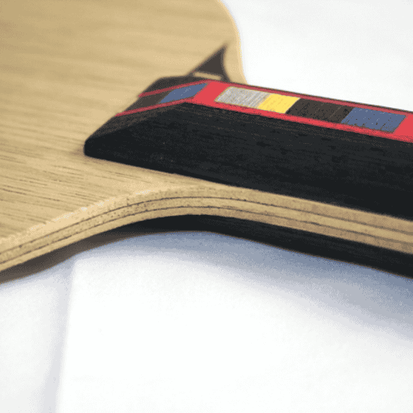 Close-up of a table tennis paddle with a black handle and red, yellow, and blue accents on a white background.